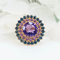 Close-up view of the Floral Radiance Ring, featuring a round silver ring plated with gold and a floral design made up of sapphire and amethyst gems surrounding a central violet amethyst.