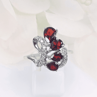 Close-up view of the Blazing Swirl Ring, featuring four pear-shaped deep red garnet gemstones in a swirling pattern, set in an intricately detailed silver band